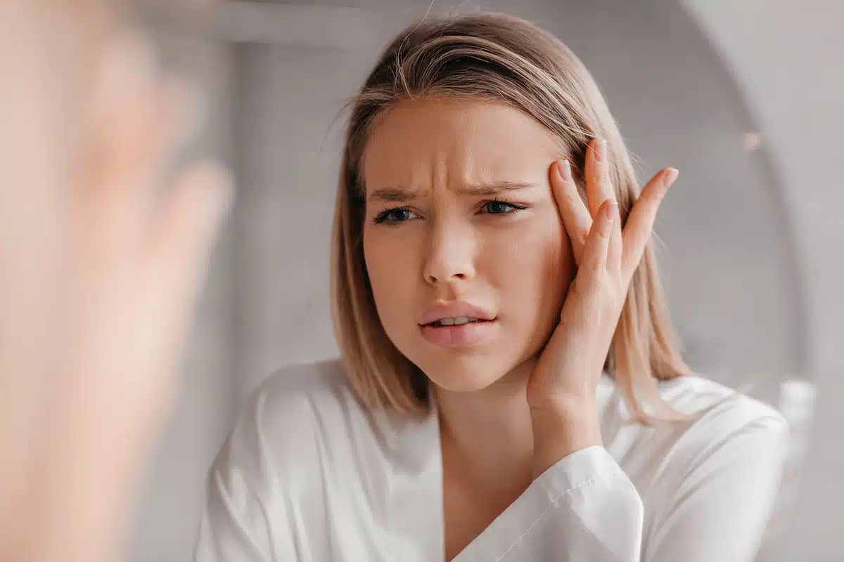Mirror reflection of upset lady looking at mirror and touching her forehead