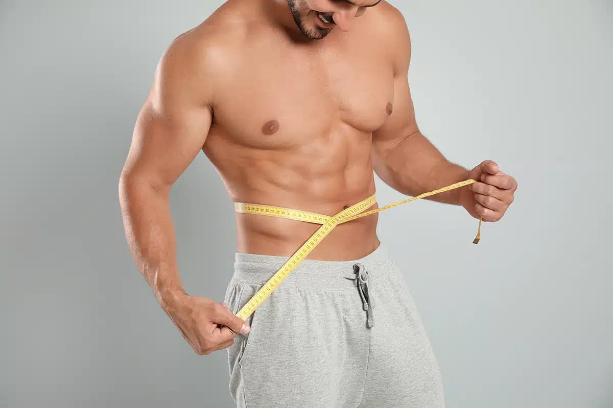 Young man with slim body using measuring tape