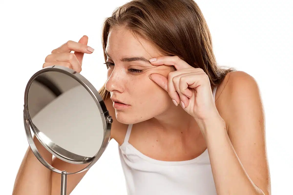 Young woman checking her wrinkles on her eyes Young woman checking her wrinkles on her eyes